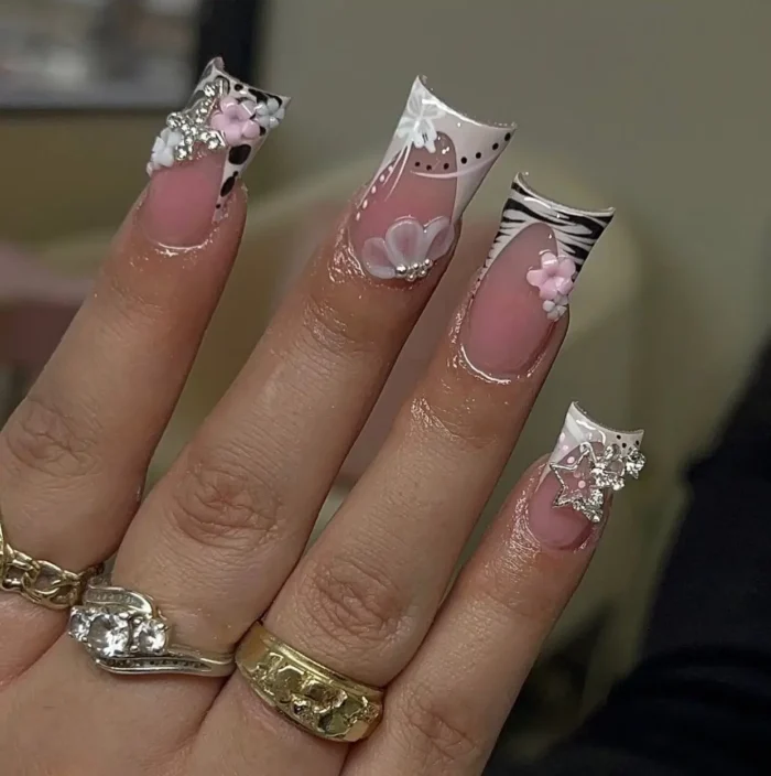 Long sculpted French tip nails with a creative mix of animal prints, 3D flower embellishments, and sparkling charm details.