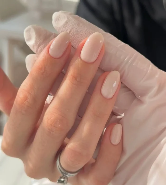 Close up of manicured hand with oval shaped nails painted in a glossy sheer pale pink nude polish.