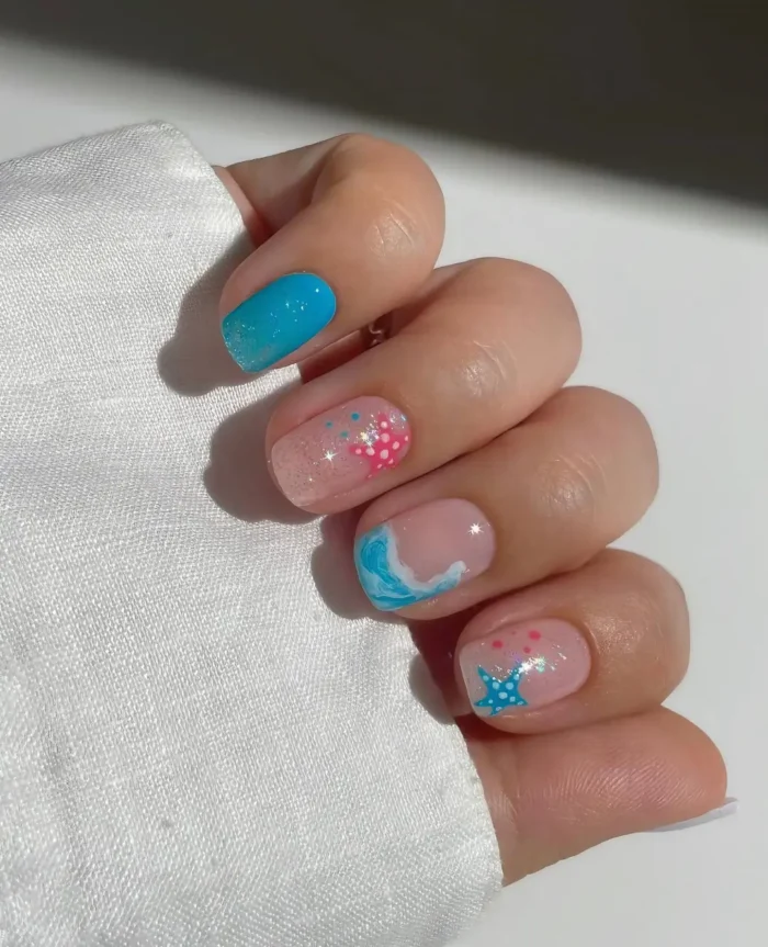Very short nails with a mixed beach theme design including solid turquoise, glitter pink with dots and starfish, and an ocean wave.