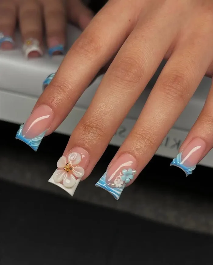 Tapered square nails showcasing a blue and white wavy French tip design, elegantly accented with 3D floral embellishments.