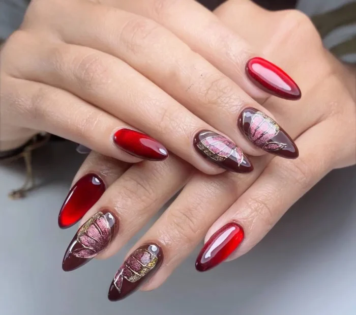 Almond nails alternating between glossy ruby red and a dark base with detailed pink and gold botanical floral designs.