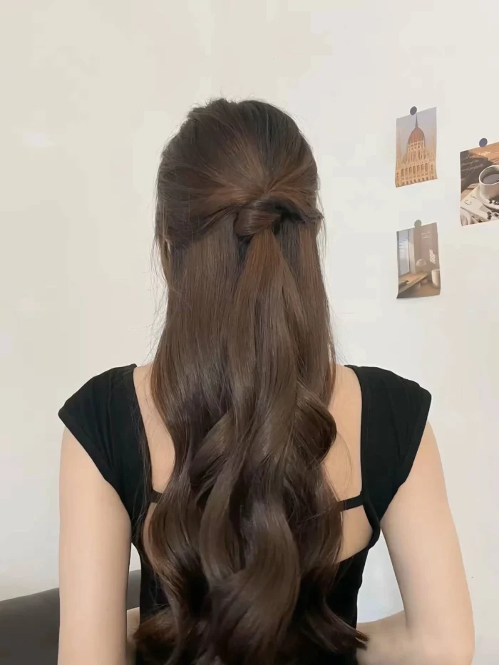 Rear view of long, dark wavy hair in a simple half-up hairstyle secured with an elegant knot-like twist.