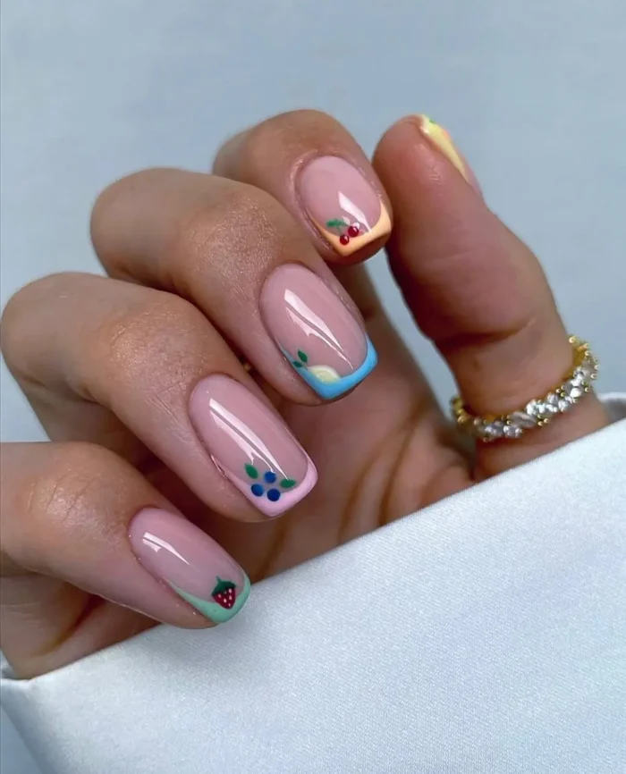 Short, neatly rounded nails with a delicate micro French manicure, each tip a different pastel color adorned with a tiny, intricate fruit design.