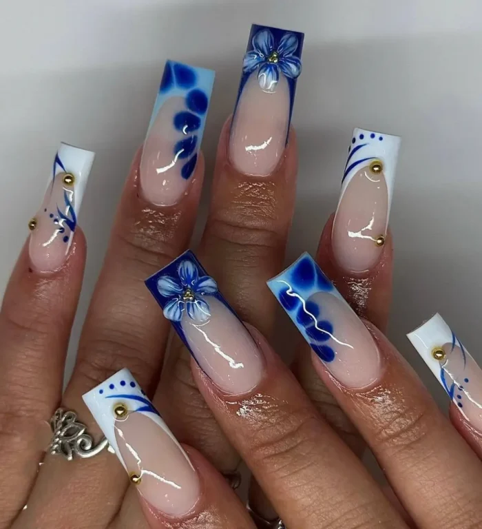 Elegant summer nail idea in blue and white on long slim square nails, featuring 3D flowers, abstract swirl tips, and gold bead accents.