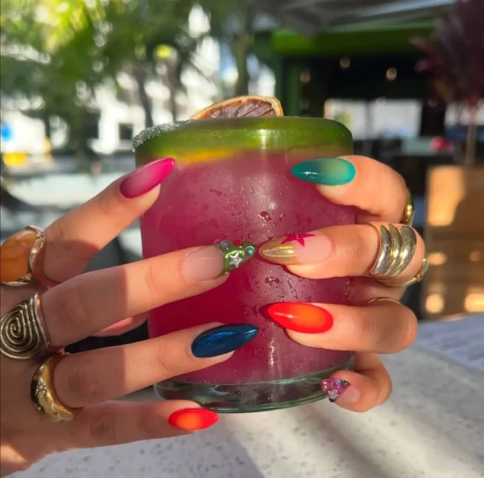 Long almond nails with a mix-and-match design including bright colorful ombres, solid navy, gold chrome accents, and colorful gem clusters.