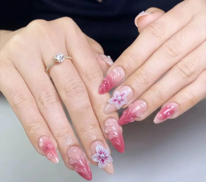 Long stiletto nails with elaborate 3D sculpted designs including pink waves, white and pink floral blooms, and raised droplet effects.