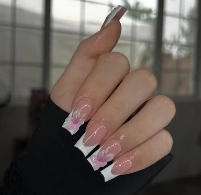 Long square nails with a classic white French manicure, beautifully adorned with softly painted pink and white flowers with green leaf accents.