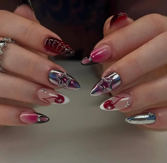 Stiletto nails featuring a Y2K-inspired mix including silver chrome with star charms, black and pink aura nails, and cherry designs on French tips.