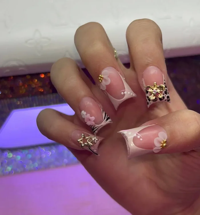 Extravagantly adorned long sculpted French tip nails featuring mixed animal prints, large gold star and floral charms, and delicate 3D flower details.