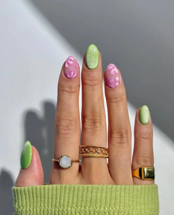 Short oval nails alternating between shimmery lime green and a sheer pink base with abstract pink floral designs.