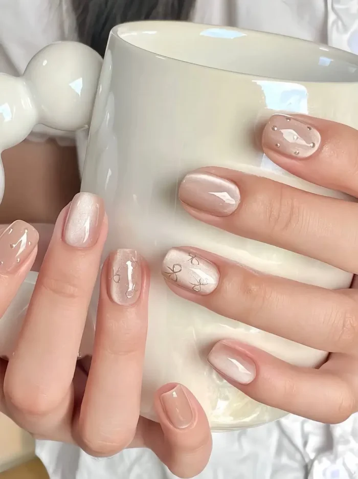 Cute simple gel nails in nude and pearlescent shimmer, with delicate bow outline art and tiny pearl dot accents.
