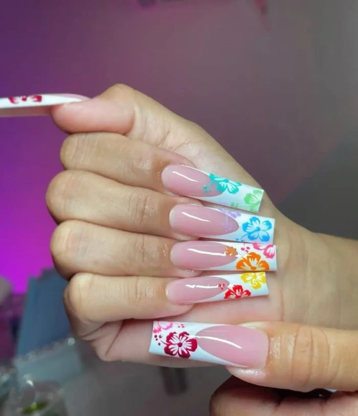Long square nails with a classic white French manicure, adorned with brightly colored, hand-painted hibiscus flowers in various vibrant shades.