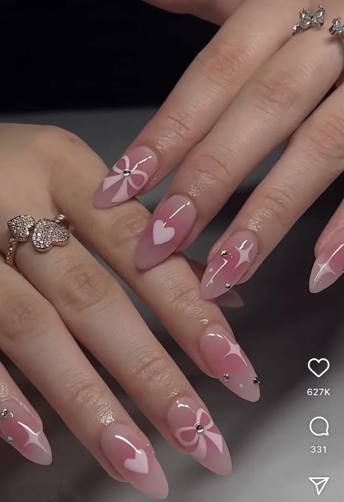 A romantic coquette-style manicure on almond nails, featuring sheer pink polish, soft-focus hearts, and delicate 3D white bows—a very cute nail idea.