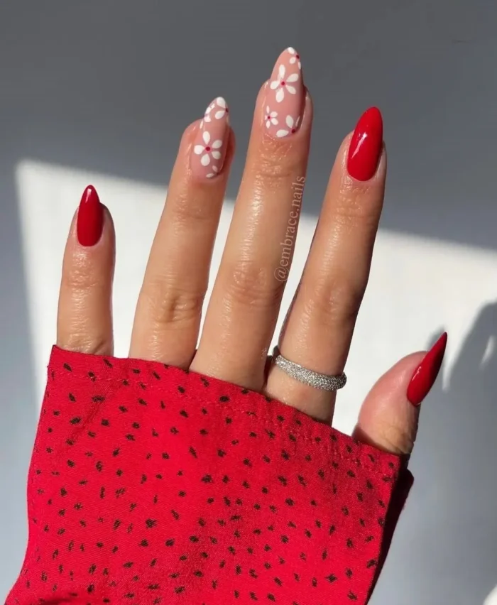 A chic, mix-and-match red nail design with solid red almond nails and accent nails featuring a white daisy floral print.