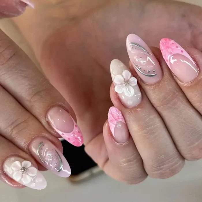 Almond-shaped nails with a milky pink base, delicate 3D white flowers, and silver accents.