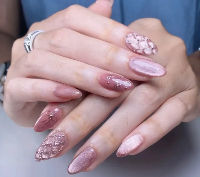 Almond nails in dusty rose and shimmery pink featuring cat-eye effect, 3D bows, line art, and textured quilted silver bead designs.