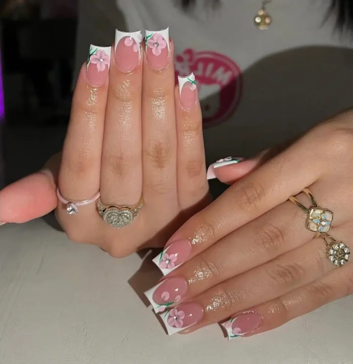 Medium-length square nails with a classic white French manicure, elegantly decorated with small, hand-painted pink flowers and green leaf accents.