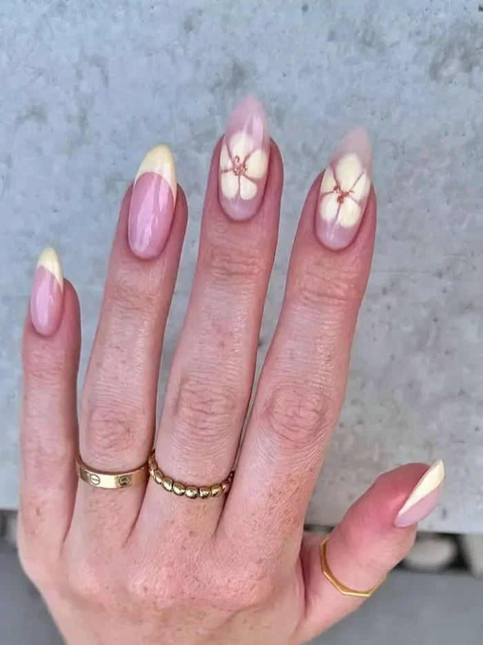 A butter yellow French manicure on almond nails, accented with large, pale 3D flowers with gold bead centers.