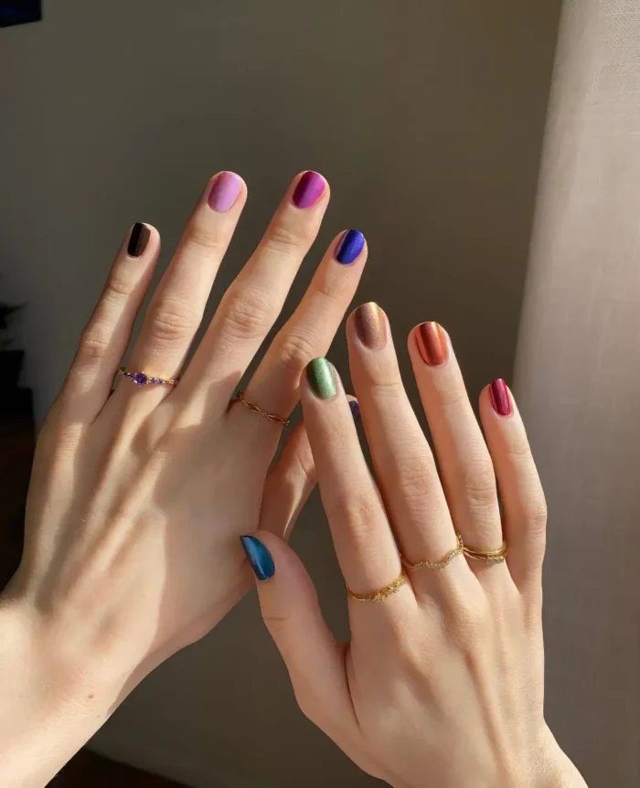 Short to medium-short rounded nails with a skittle manicure featuring a different metallic or chrome polish color on each nail.
