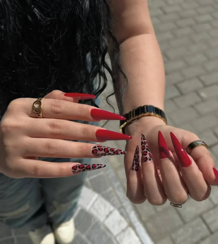 A bold red nail design on long stiletto nails, featuring a mix of solid red and a detailed red and black leopard print.