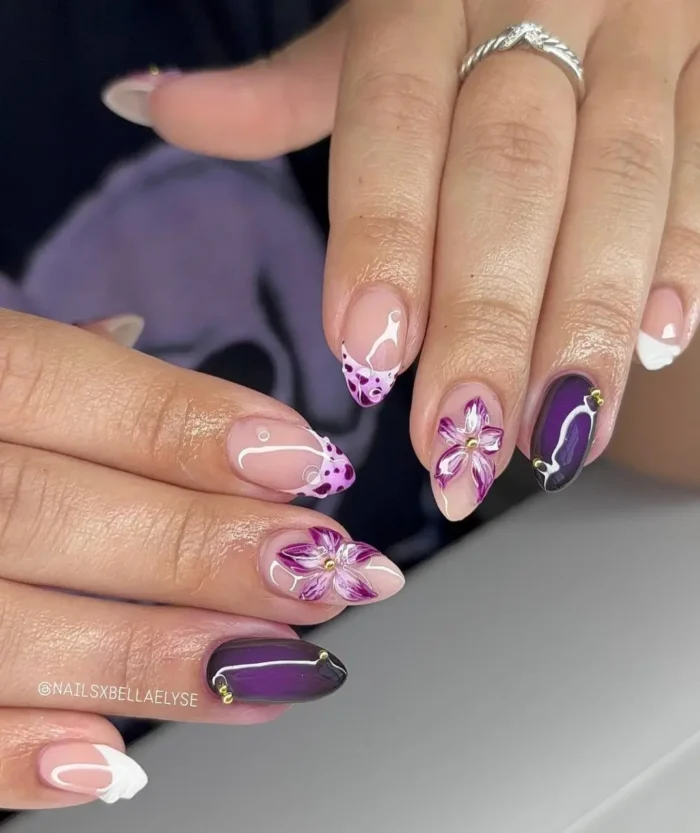 Artistic purple nail design with painted purple orchids on almond nails, accented with deep plum and gold beads.
