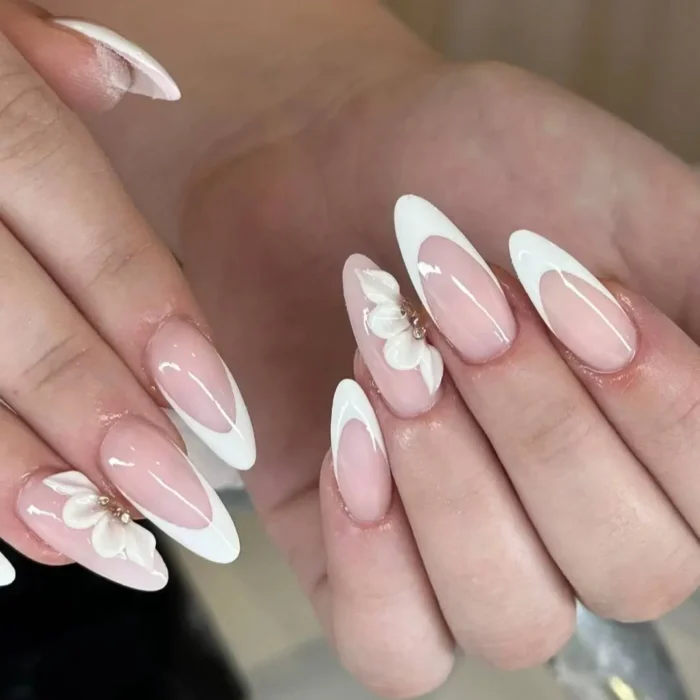 An almond French manicure with a white 3D flower accented with a gold bead, placed at the cuticle.