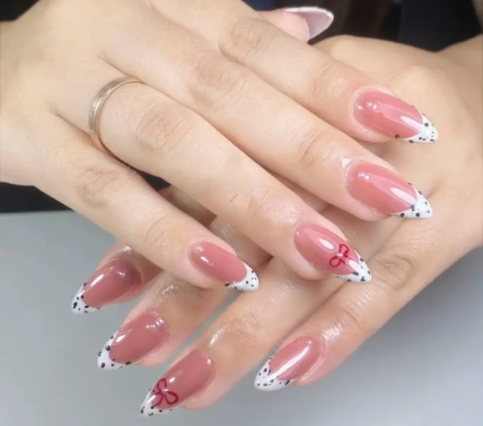 Almond-shaped nails with a dusty rose base and sharp V-shaped French tips featuring a white and black Dalmatian spot pattern and red bow details.