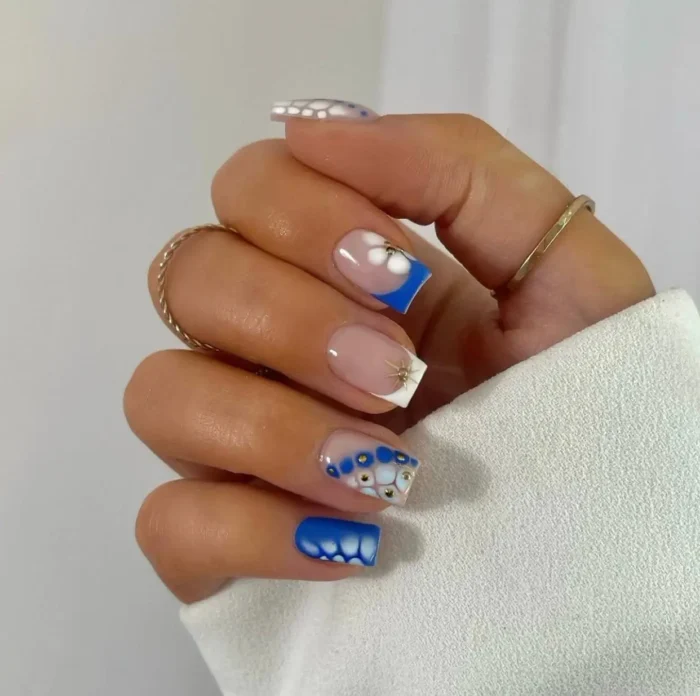 Short square nails with a modern blue and white French manicure for summer, featuring floral dot art and gold accents.