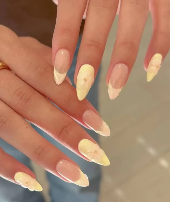 A manicure on almond-shaped nails combining textured butter yellow French tips and full butter yellow nails with 3D floral details.
