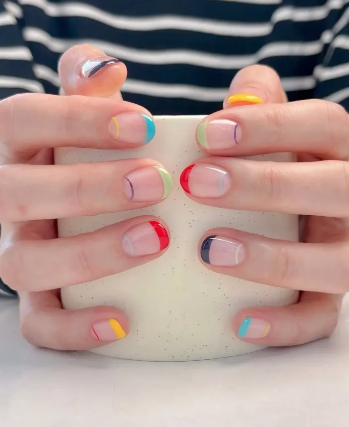 Short rounded nails with a sheer nude base and a very thin micro-French tip painted a different bright color on each nail.
