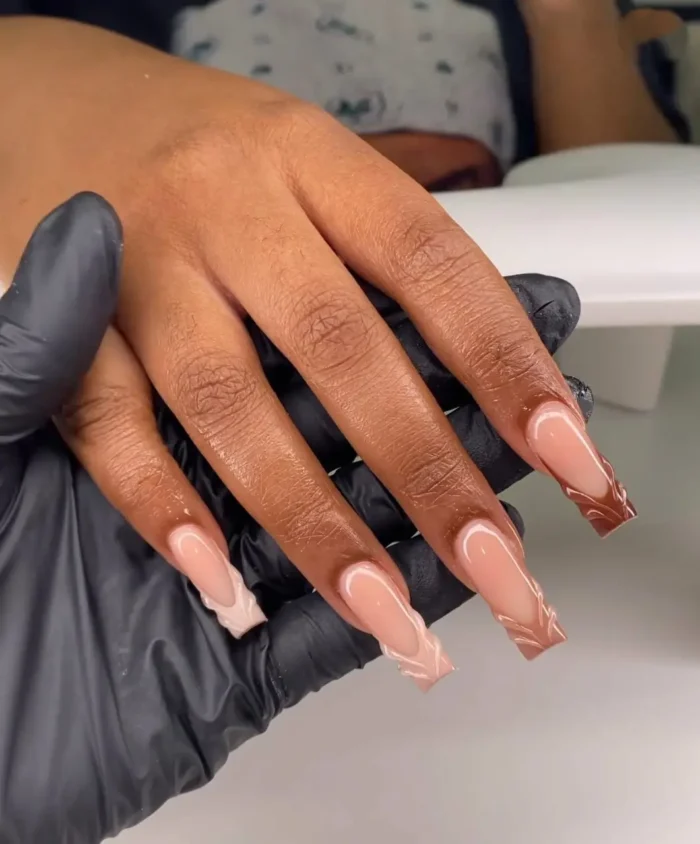 Long coffin nails with a nude to brown ombré and abstract caramel and chocolate brown swirl designs on the tips.