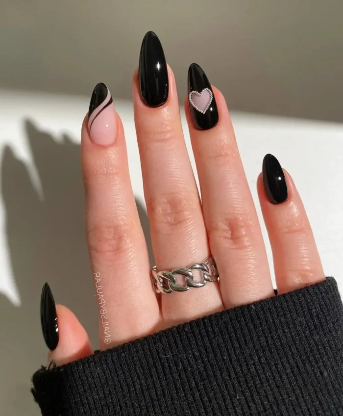 Almond-shaped nails primarily in glossy black, with accent nails featuring a black swirl on sheer pink and a pink heart on black.