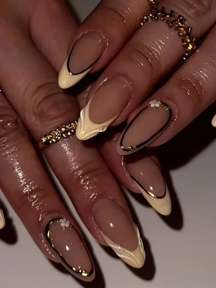 A sophisticated manicure on almond nails with sculpted butter yellow French tips and framed accent nails with 3D floral details.