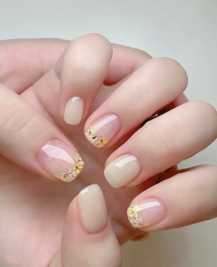 Short rounded nails with mixed sheer nude and milky white bases, featuring tiny pressed yellow and white flowers arranged along the tips.