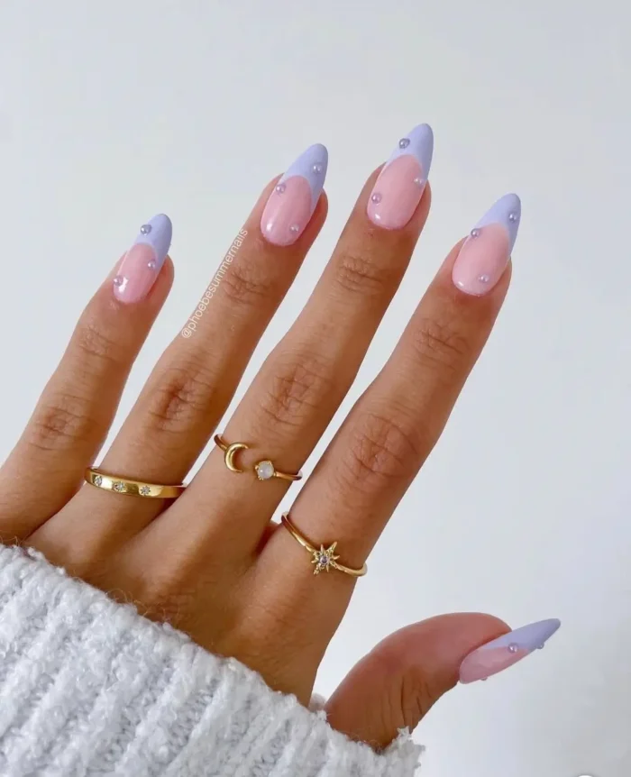 Long almond nails with a natural pink base, soft lavender French tips, and delicate iridescent pearl embellishments.
