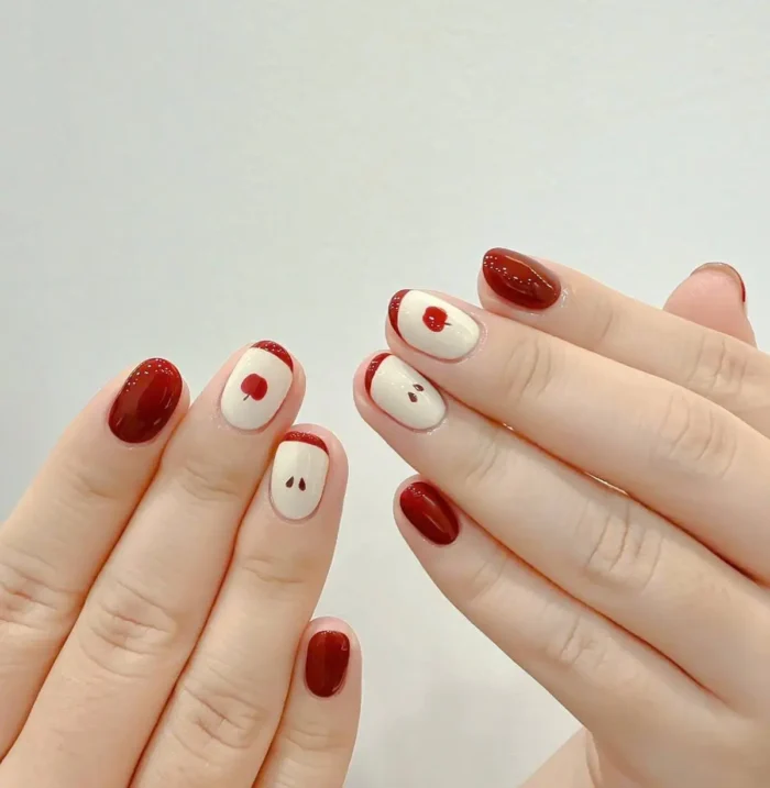A minimalist and cute apple-themed nail design featuring a crimson cuff and tiny seed details on a sheer, negative space background.