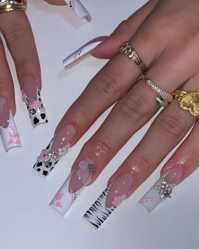 Eclectic long square nails showcasing a mix of black and white cow and zebra prints, contrasted with soft pink 3D flowers, painted pink bows, and sparkling gem accents.
