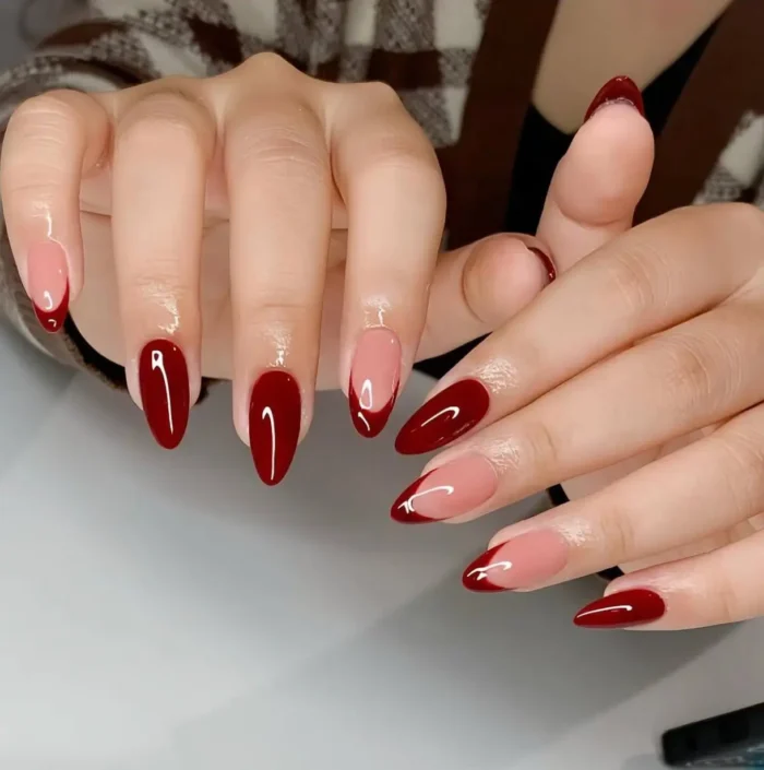 A sophisticated red nail design featuring a modern mix of solid deep red nails and an asymmetrical side-French manicure.