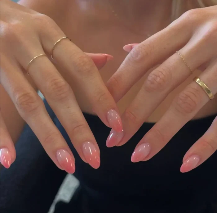 Cute simple gel manicure with a soft warm coral pink aura blush effect on medium almond-shaped nails.