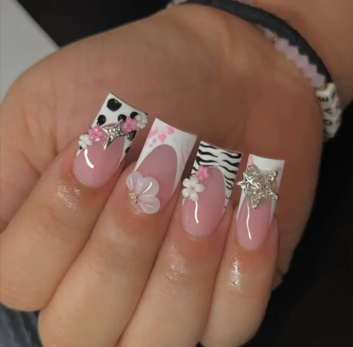 Long sculpted square nails with an eclectic mix of French tips, including cow print with a silver bow, zebra print with 3D flowers, and a star charm.