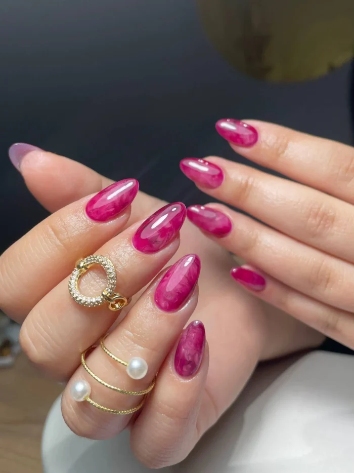 Medium-long almond-shaped nails with a glossy magenta and fuchsia pink marbled gemstone effect.
