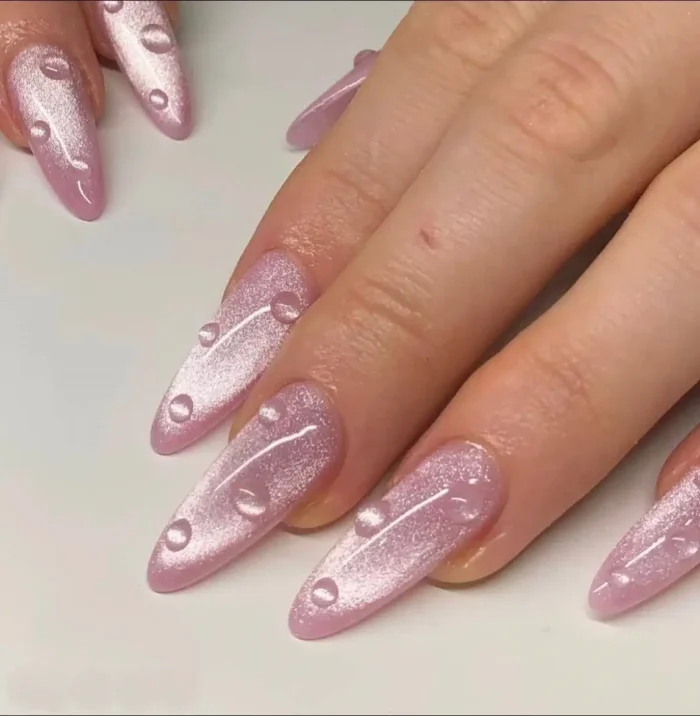 Cute simple gel nail idea with a light pink shimmery cat-eye effect and 3D clear gel water droplet accents on long pointed nails.