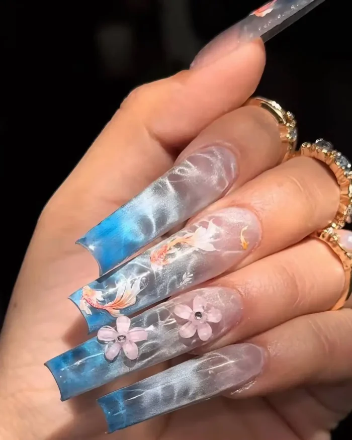 Long, sculpted translucent nails with a blue and white watery background effect, adorned with delicate painted florals and 3D pink flower accents.