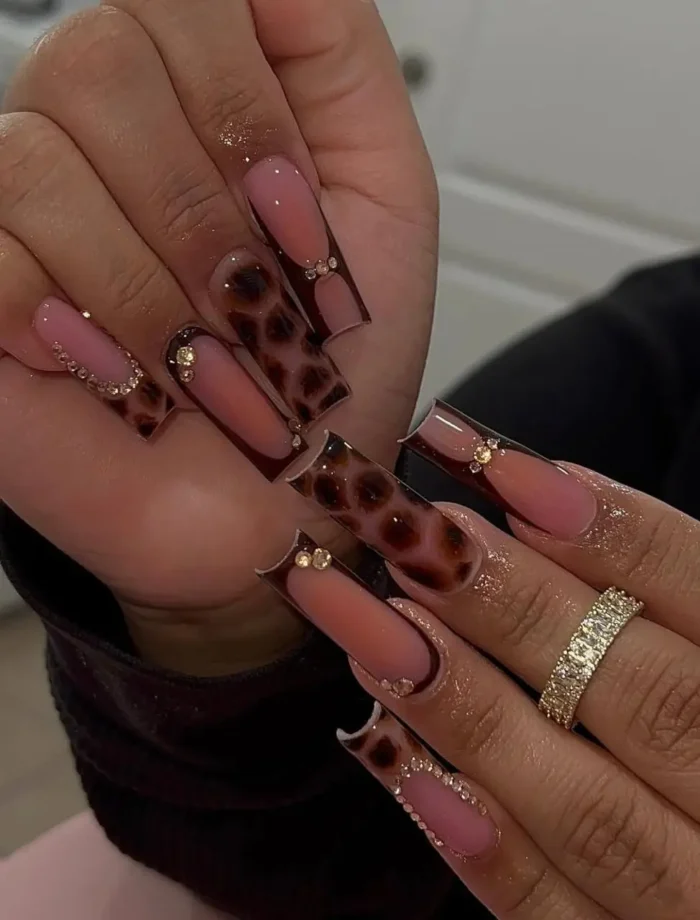 Long square nails with glossy tortoiseshell patterned French tips, accented with a line of tiny gold rhinestones.