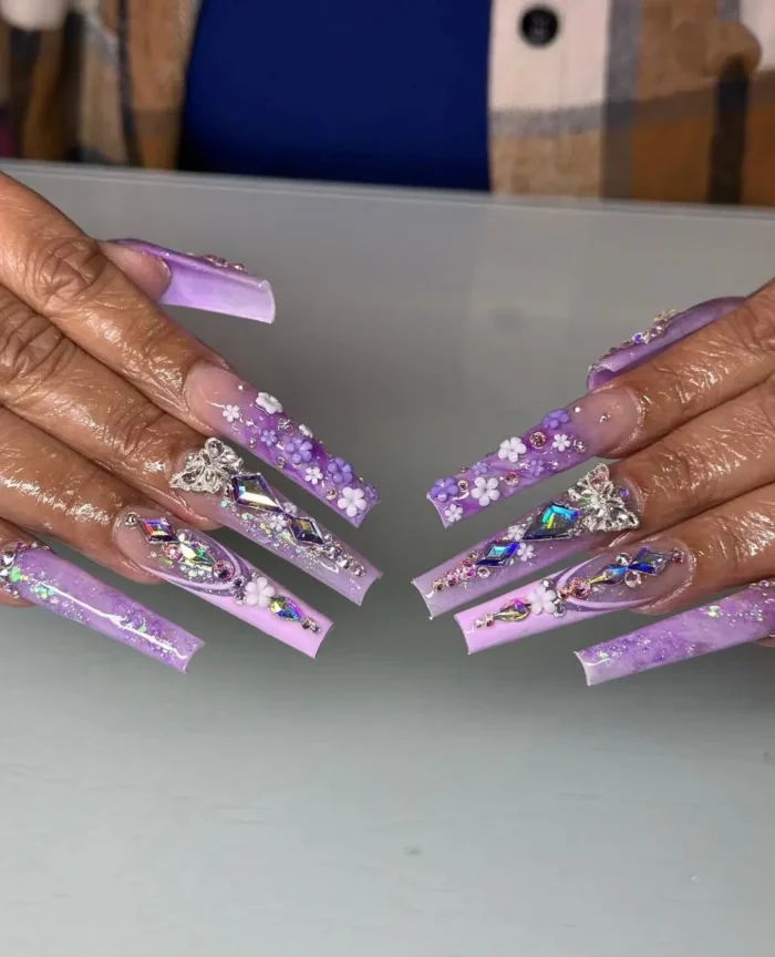 Extra-long nails with jubilee jewel tones, a freestyle purple nail design with 3D florals, crystals, and butterfly charms.