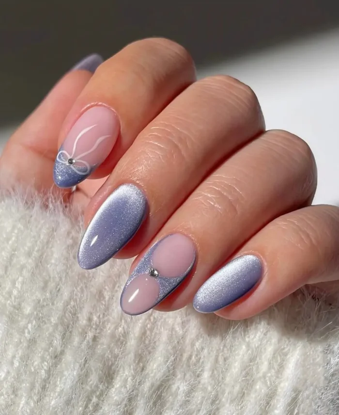 A modern and chic manicure with periwinkle cat-eye nails paired with a sheer accent nail featuring a hand-painted bow.