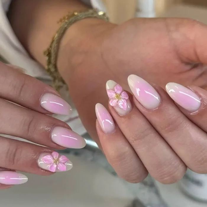 Almond nails with a baby pink aura effect, adorned with delicate 3D pink flowers with gold bead centers.