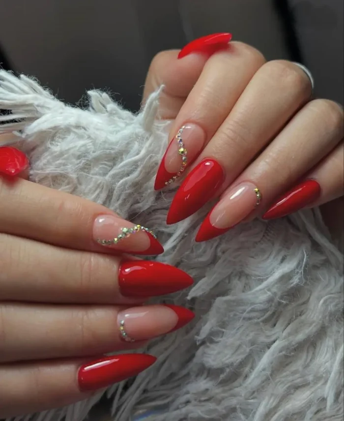 A glamorous red stiletto nail design featuring a V-tip French manicure accented with a delicate curve of rhinestones.