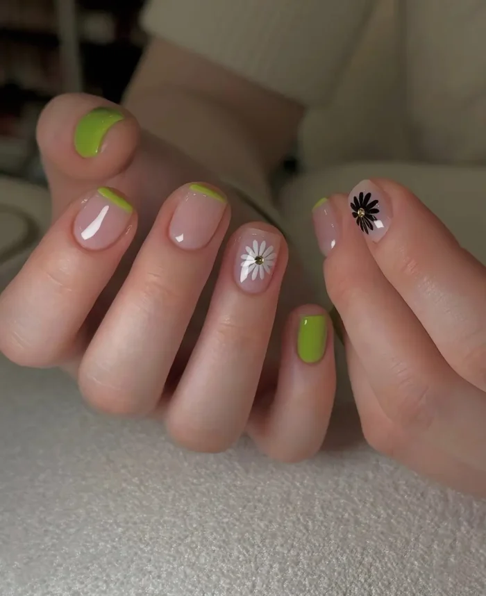 Short square nails with a sheer nude base featuring lime green French tips, a solid lime green pinky nail, and simple daisy flower accents.