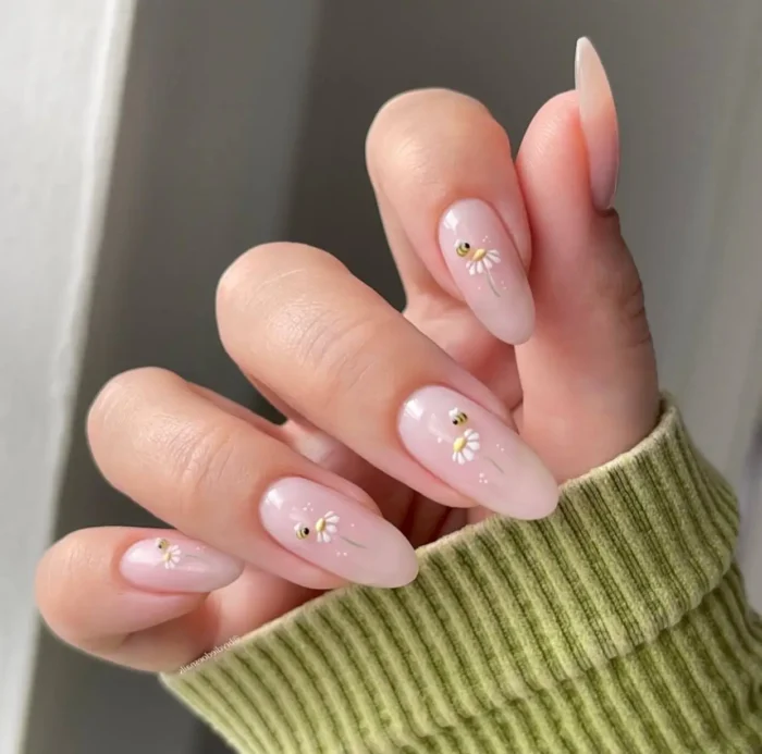 Long almond nails with a sheer milky pink base featuring small white daisy designs, each accented with a tiny gold stud center.